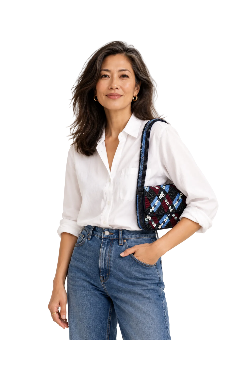 A woman wearing a white button-down shirt and blue jeans, carrying a small black shoulder bag with a colorful geometric pattern and a dark blue strap, set against a plain white studio background.