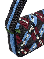 Close-up of a beaded shoulder bag with a geometric pattern of black, light blue, burgundy, and white floral beads, featuring a wide black and light blue beaded strap.