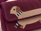 A close-up of a beaded shoulder bag in deep burgundy with a dachshund design on the flap. The bag features intricate beadwork in burgundy, beige, brown, navy, and white, with a matching burgundy strap visible in the upper left corner.
