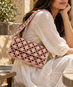 A woman in a white embroidered dress carries a pink and beige embroidered shoulder bag with a floral pattern in an outdoor setting.