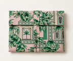 A folded piece of fabric or textile with a pink background and a green tropical botanical print, arranged flat against a light beige background.