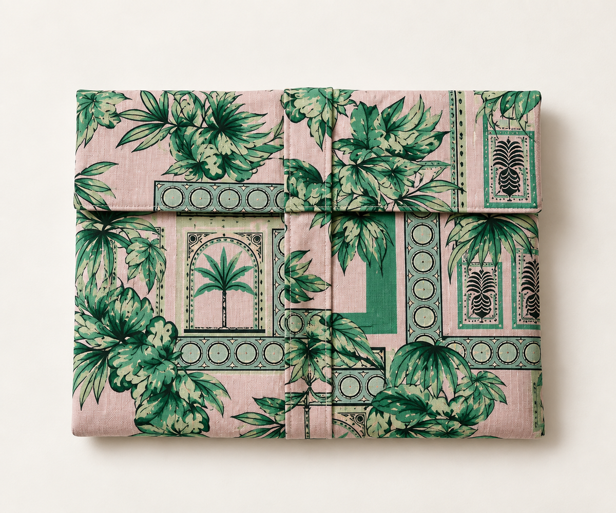 A folded piece of fabric or textile with a pink background and a green tropical botanical print, arranged flat against a light beige background.