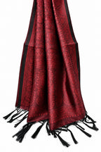 A red and black patterned shawl with black tassels, draped against a solid white background.