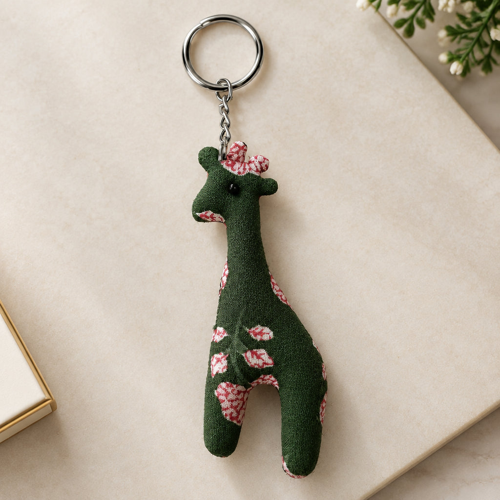 A small fabric giraffe keychain charm with a dark green body and pink floral pattern, attached to a silver metal split ring, shown on a plain light background.