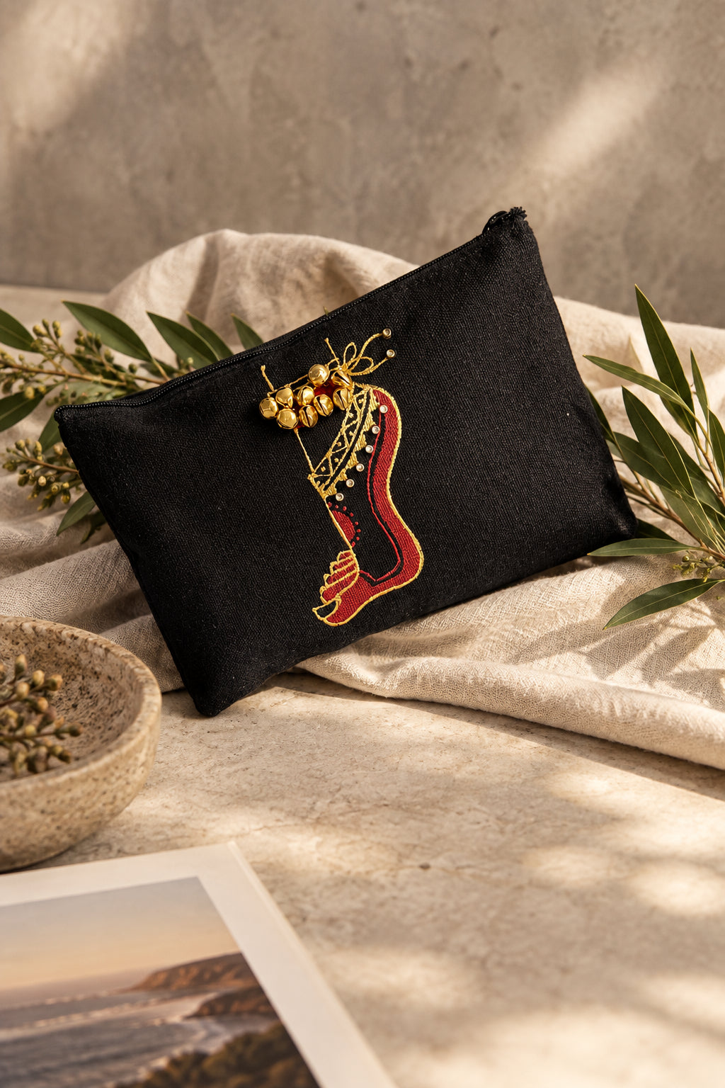 A black fabric pouch featuring an embroidered red and gold harp design, styled with green leaves on a plain white background.