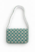 A small fabric shoulder bag with a blue and beige checkered patterned body and a white fabric strap, laid flat on a light beige surface.