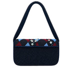 A dark navy blue shoulder bag with a wide, patterned top flap featuring geometric and floral designs in red, blue, white, and black, set against a white studio background.