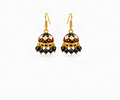 A pair of gold-toned traditional Indian jhumka earrings with black, cream, and maroon enamel detailing and dangling black beads, shown on a light cream background.