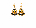 A pair of traditional Indian gold-plated jhumka earrings with black and white enamel patterns, dangling black beads, and small gold bead accents, set against a plain light beige background.